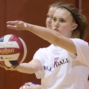 Female player holds volleyball in front of her in preparation to serve
