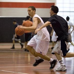 A man dribbles a basketball while running from a member of the other team