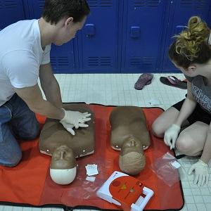 A student performs CPR on a dummy while another student observes