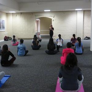 Students sit in lines and follow the directions of the yoga instructor leading them