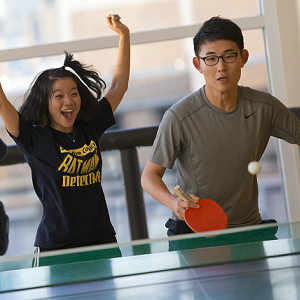 A girl cheers beside a boy who is playing table tennis