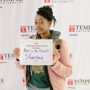 photo of Temple student with sign that reads: “I love the Libraries because ‘Chat in the Stacks’ is amazing.
