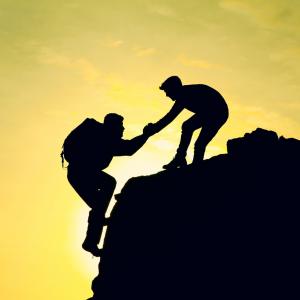 A man helping another man climb a mountain. 
