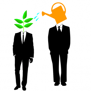 Two people in suits standing next to each other, one has a plant as a head and one has a watering can instead of a head to symbolize mentoring. 