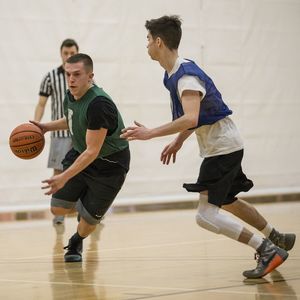 A basketball player tries to dribble around his defender while a ref watches in the background.