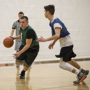 A basketball player attempts to dribble around his defender while a ref watches in the background of the photo.