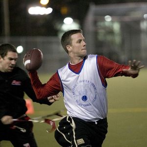 A flag football QB throwing the ball as a defender tries to pull his flag.