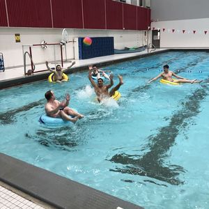 An inner-tube water polo player reaches to catch a pass that was thrown over the top of the defense.