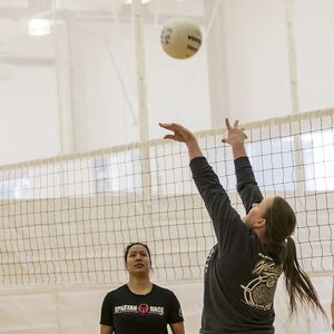 A volleyball players setting up the ball for a teammate next to the net.