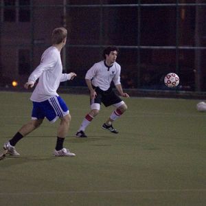 Players playing soccer at night on a turf field.