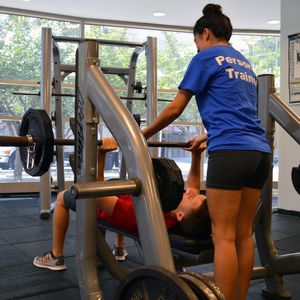 A personal trainer spots a client who is bench pressing.