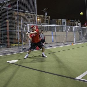 A batter preparing to swing at an incoming softball pitch.