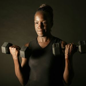 A woman lifting weights in front of a black background.