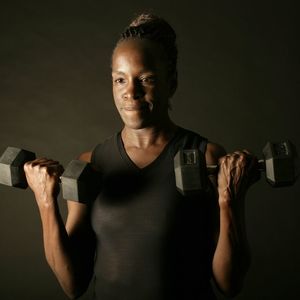A woman lifting weights in front of a black background.