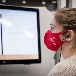 Student sitting at computer with Temple mask