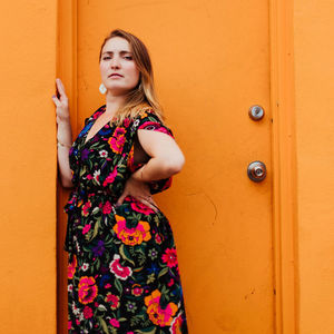 woman in a floral dress standing in front of a bright orange doorway