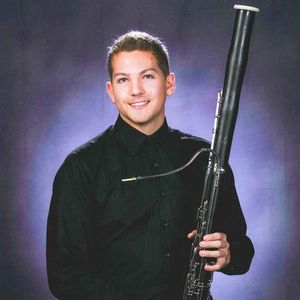 smiling man with brown hair and a black shirt holding a bassoon