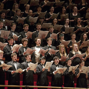 dozens of singers, dressed in formal black, singing and holding music