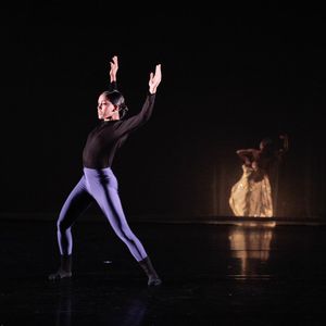 dancer in a black shirt and purple leggings against a black stage background