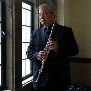 Man in a suit holding a clarinet and looking out of a window