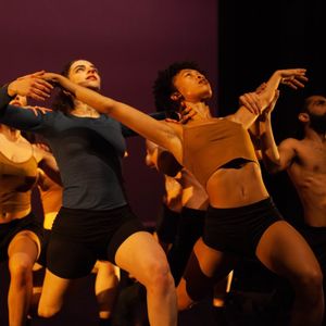 Dancers wearing brown and black posing on a dimly lit stage