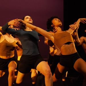 dancers wearing brown and black posing on a dimly lit stage