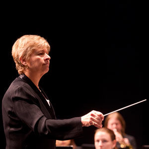 conductor in front of a band onstage, wearing black