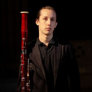 headshot of a man in a black suit holding a bassoon