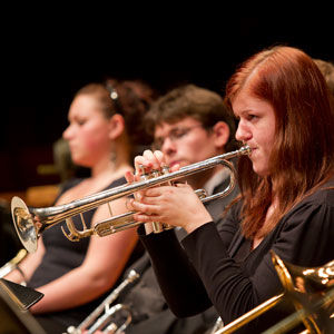 red-headed woman playing a trumpet; other band members visible but blurred in the background