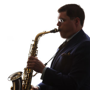 profile of a man in a suit playing a saxophone against a bright white background