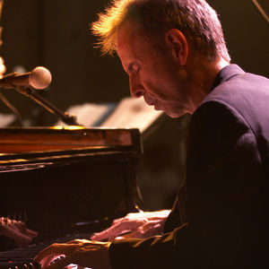 man playing piano with his eyes closed, lit by stage lighting