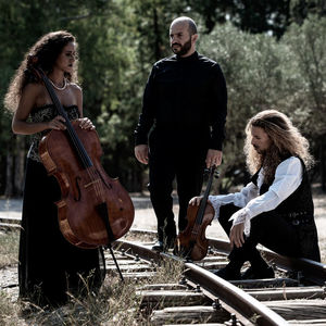 three musicians holding string instruments posed on a railroad track